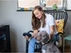 A woman is sitting in a chair with a dog, holding a portable CD player. Produktbild-Vorschau