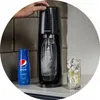 A SodaStream machine is being used to carbonate water, with a bottle of Pepsi syrup and a glass of soda with ice and lemon nearby. Produktbild-Vorschau