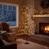 A decorative LED tree is placed in a cozy living room with a fireplace and a window showing a snowy outdoor scene. Náhled obrázku produktu