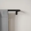 A close-up view of a black curtain rod mounted on a white wall, with a grey curtain partially visible. Podgląd zdjęcia produktu