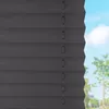 A close-up view of dark gray pleated blinds against a bright blue sky with some green trees in the background. Produktbild-Vorschau