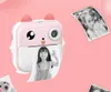 A pink mini-thermo printer with a cat-like design is shown, printing photos of children and a dog. Other printed photos are displayed around it. Produktbild-Vorschau