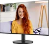 A woman is sitting on a couch in front of a monitor displaying her image. Náhled obrázku produktu