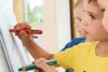 Three young children are drawing on a large sheet of paper on an easel. Voir les images du produit