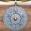 A top-down view of a decorative washbasin with a blue and white floral pattern, featuring a gold faucet. Náhled obrázku produktu