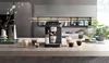 A DeLonghi coffee machine is displayed on a kitchen counter with several cups of coffee and decorative items. Voir les images du produit