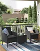 A balcony setting with a black rattan furniture set, including two chairs and a small table, placed on a striped rug. The background shows a garden with manicured bushes and a wooden fence. Produktbild-Vorschau