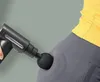 A close-up shot of a person using a black massage gun on their hip. Produktbild-Vorschau