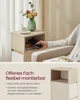 A person's hand is placing a smartphone into an open compartment of a narrow bedside table. A cup and saucer with a spoon are on top of the table, next to a vase with flowers. The lower part of the image shows a close-up of the bedside table with text desc Produktbild-Vorschau
