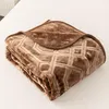 A folded brown blanket with a geometric pattern is placed on a white surface. Podgląd zdjęcia produktu