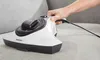 A hand is holding a handheld vacuum cleaner and cleaning a sofa. Produktbild-Vorschau