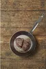 Two pieces of cooked meat are in a frying pan on a wooden surface. Náhľad obrázku produktu