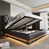 A modern bedroom with a bed that has its storage compartment open, revealing the mattress and some items inside. The bed has LED lighting around its base. Produktbild-Vorschau