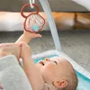 A baby is lying on a playmat and reaching for a toy. Produktbild-Vorschau