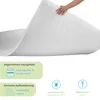 A hand is holding up a white mattress topper, showing its texture and flexibility. Below the topper are several informational graphics and text. Náhled obrázku produktu
