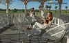 Two women relaxing in a white gazebo on a sunny day, with one woman holding a cup of coffee. Produktbild-Vorschau