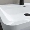A close-up view of a white sink with a black drain cover and faucet base. Produktbild-Vorschau