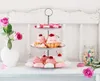 A three-tiered cake stand filled with pink cupcakes, meringues, and small cakes, next to a vase of pink roses and a jar of colorful candies. Náhľad obrázku produktu
