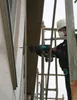 A person is using a power drill on the side of a building, with scaffolding in the background. Produktbild-Vorschau