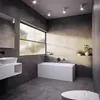 A modern, spacious bathroom with a bathtub, sink, and toilet, illuminated by natural light from a large window. Produktbild-Vorschau