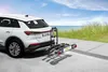 A white car with a bike rack attached is parked on a paved surface near a beach. Anteprima dell’immagine prodotto