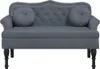 A dark gray velvet sofa with decorative nailhead trim and two round throw pillows, shown from the front on a white background. Náhled obrázku produktu