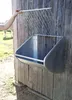 A person's hand is shown opening a metal hay feeder mounted on a wooden wall. A white horse is visible in the background. Anteprima dell’immagine prodotto