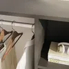 A close-up view inside a wardrobe, showing clothes hanging on a rail and books on a shelf. Náhled obrázku produktu