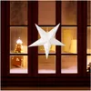 A white paper star lantern with small yellow cutouts is hanging in a window at night. Náhled obrázku produktu