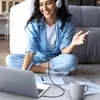 A woman is sitting on the floor with a laptop and headphones, working or studying. Produktbild-Vorschau