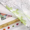 A close-up view of a fabric with a floral pattern, partially covering a book or magazine with text and small decorative items. Produktbild-Vorschau