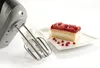 A hand mixer is shown next to a slice of cake and a bowl of whipped cream. Produktbild-Vorschau
