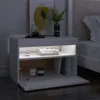 A modern white nightstand next to a bed, with a painting and a plant on top, and books, candles, and a small plant inside the open compartment. Produktbild-Vorschau