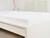 A white bedsheet is laid out on a white bed frame, with a white slatted headboard in the background. Náhled obrázku produktu