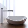 A white faucet and a white basin are shown on a wooden surface, with a blurred white curtain in the background. Náhled obrázku produktu
