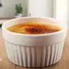 A close-up shot of a crème brûlée in a white ramekin, placed on a wooden surface. Produktbild-Vorschau