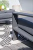 A close-up view of a modern outdoor furniture set, focusing on the armrest and cushion of a chair, with a patterned rug and wooden decking visible. Produktbild-Vorschau