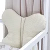 A close-up view of a cream-colored, waffle-textured pillow shaped like a butterfly, placed inside a white crib. Produktbild-Vorschau