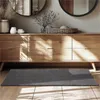 A dark gray rug is placed on a wooden floor in front of a wooden dresser with decorative items on top. Produktbild-Vorschau