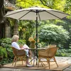 A woman sits at a table under a large umbrella in a garden setting, reading a book. Produktbild-Vorschau