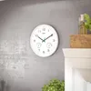 A white wall clock with a thermometer and hygrometer is mounted on a gray wall. Voir les images du produit
