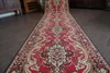 A long red carpet runner with a traditional pattern is laid out on a dark wooden floor in a room with wooden furniture. Produktbild-Vorschau