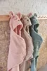 Three hooded blankets with animal faces hanging on a wooden rack against a brick wall. Voir les images du produit