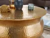 A close-up view of a gold hammered coffee table with decorative items on top. Produktbild-Vorschau