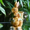 A decorative statue of two rabbits, a mother and child, in a garden setting. Produktbild-Vorschau