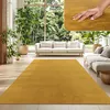 A living room with a large window overlooking a garden, featuring sofas and a large yellow rug. Produktbild-Vorschau
