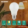 A Sylvania LED light bulb is shown in the foreground, with a blurred background of a plant and a lamp. Produktbild-Vorschau