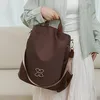 Brauner diebstahlsicherer Rucksack mit silbernem ineinandergreifendem Logo, gehalten von einer Person in einem hellgrünen Hemd und weißem Rock Anteprima dell’immagine prodotto