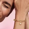 A close-up shot of a person's wrist wearing a gold charm bracelet with a pearl sun charm. Produktbild-Vorschau