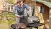 A man is cleaning a barbecue grill in a backyard setting. Anteprima dell’immagine prodotto